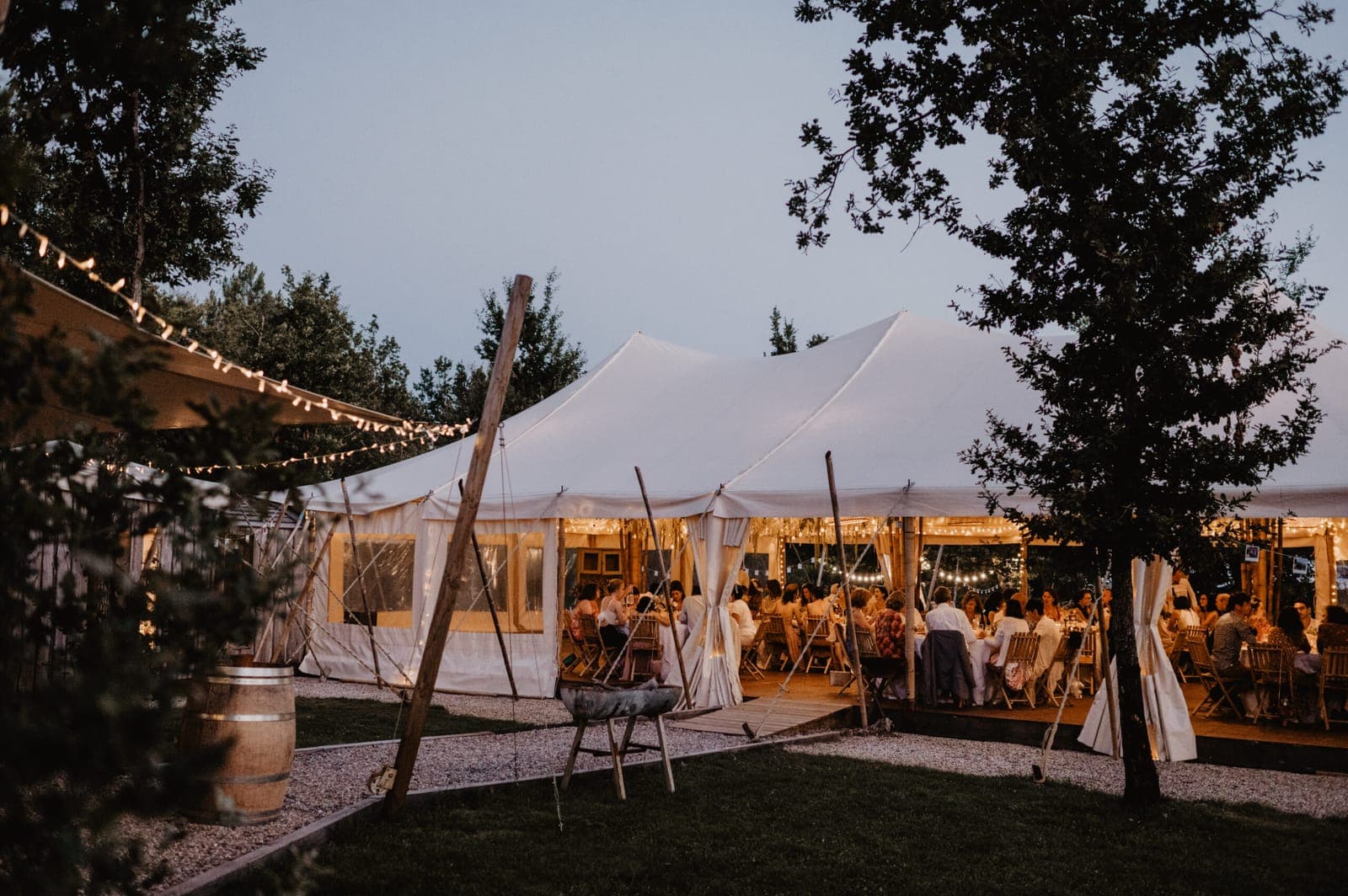 Dîner sous chapiteau à la tombée du jour, guirlandes allumées et tables dressées.